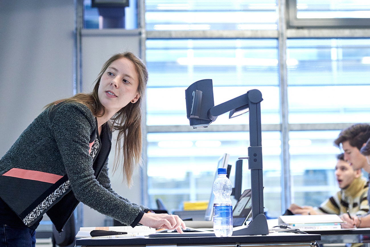 Eine Studentin des Instituts Sekundarstufe II unterrichtet in einem Praktikum an einem Gymnasium. Sie steht am Hellraumprojektor. Vor ihr sind einige Schüler zu sehen.