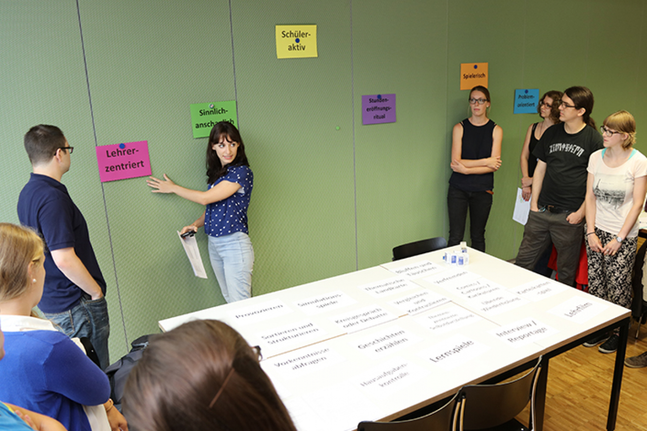 Studierende des Instituts Sekundarstufe II im Seminar Allgemeine Didaktik. Eine Studentin steht an einer Magnetwand, an der Zettel mit Überschriften wie „Lehrerzentriert“ hängen und erklärt etwas.