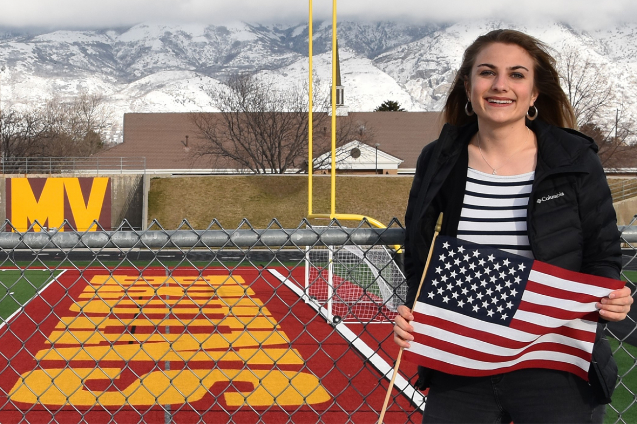 Die PHBern-Studentin Isabelle Keller, die ein Praktikum in Orem (Utah) absolviert hat. Sie steht auf dem Football-Feld der Schule und hält eine Flagge der U.S.A. in den Händen.