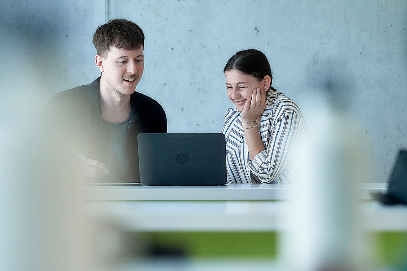 Zwei Studierende bei einer Besprechung. Vor ihnen steht ein Laptop.
