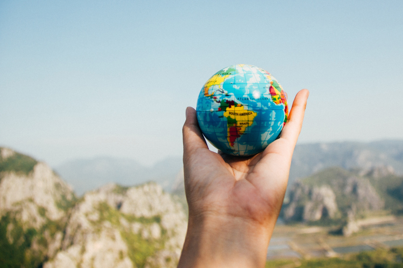 Jemand hält eine Weltkugel in der Hand auf einem Aussichtspunkt