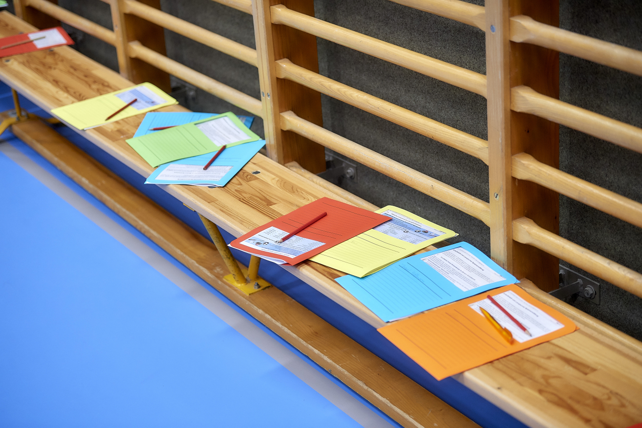 Arbeitsmappen mit Blättern sind auf einer Turnbank in der Turnhalle aufgereiht.