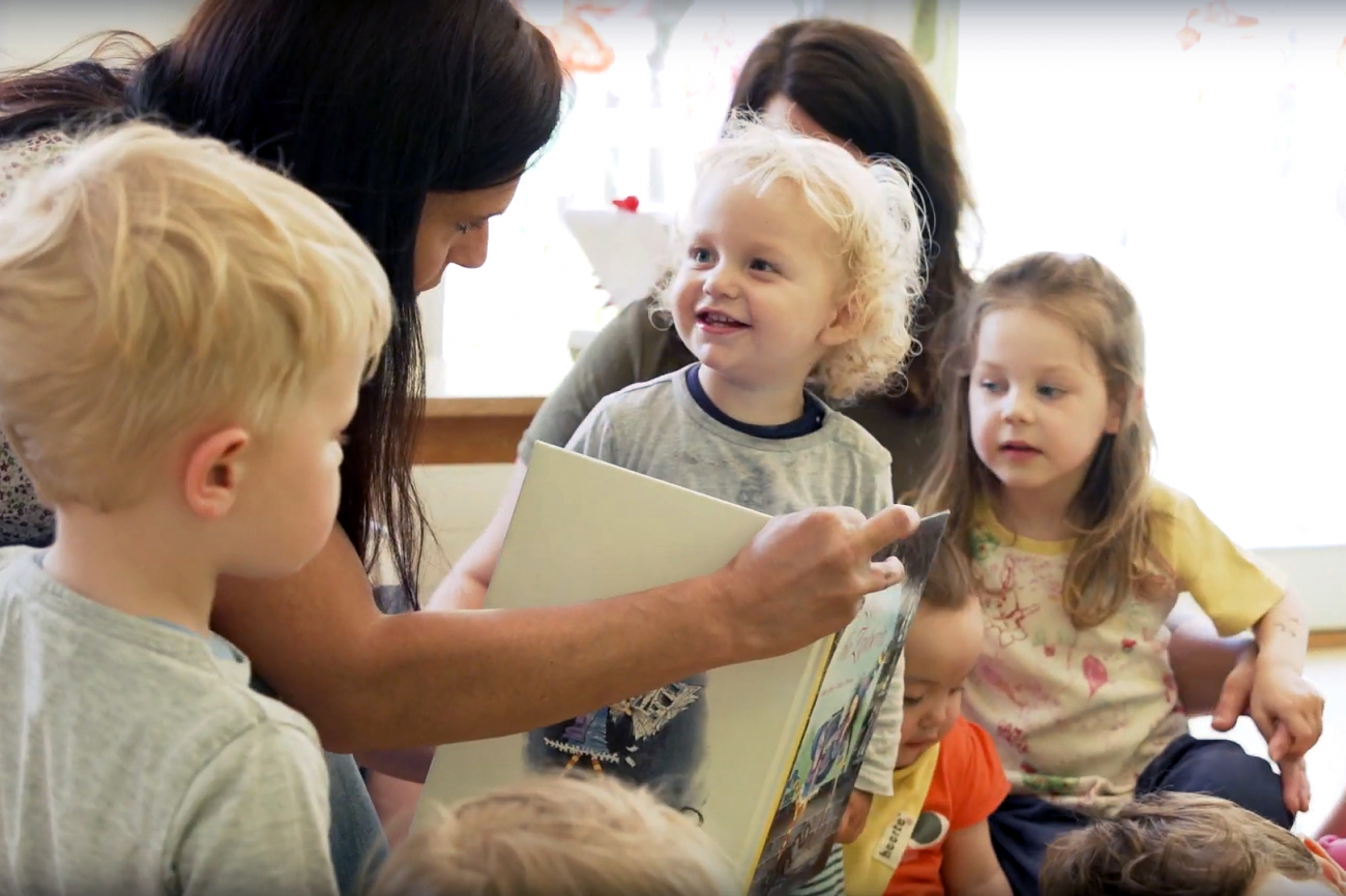 Eine Leiterin erklärt den Vorschulkindern ein Bilderbuch.