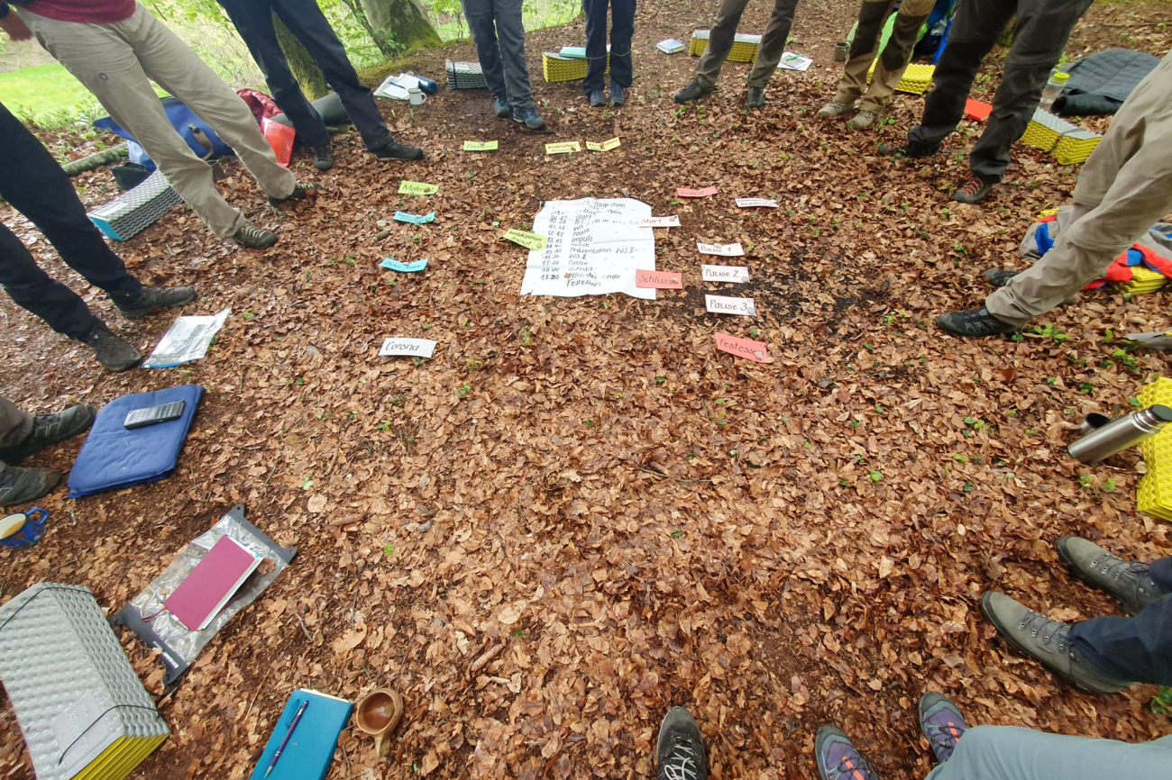 Kursteilnehmende stehen im Kreis im Wald