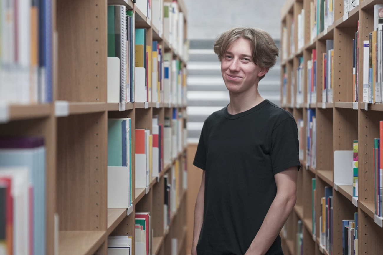 Lucas steht zwischen zwei Regalen in der Bib