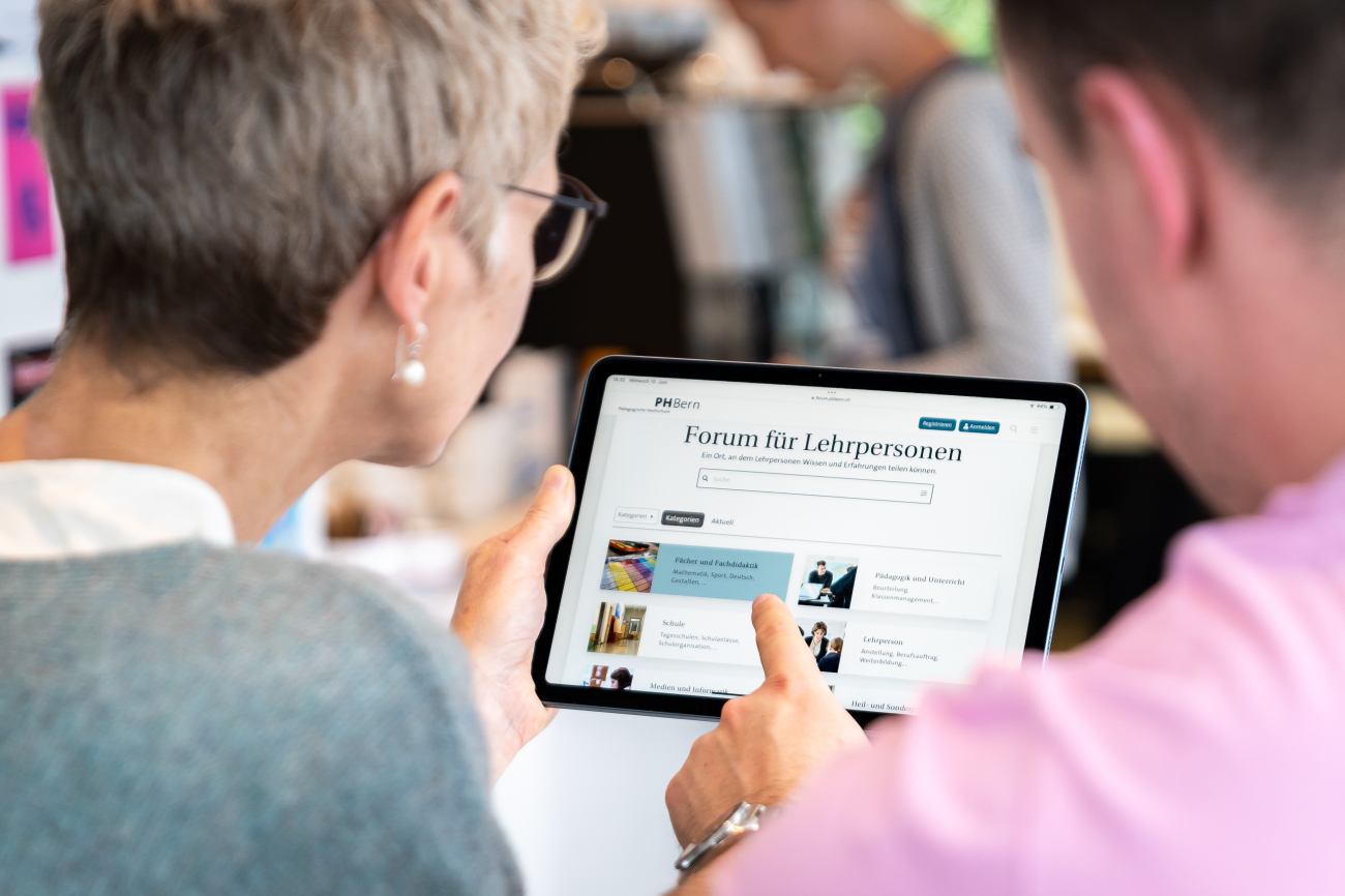 Frau und Mann schauen gemeinsam auf ein Tablet, zu sehen ist der Screen des Forums für Lehrpersonen