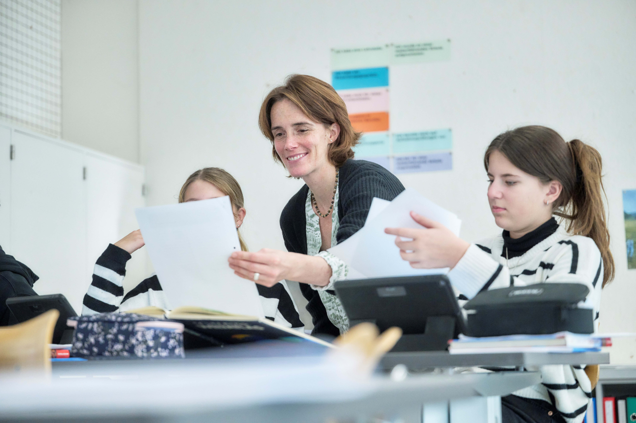 Lächelnde Lehrerin bespricht Arbeisblätter mit zwei Schülerinnen