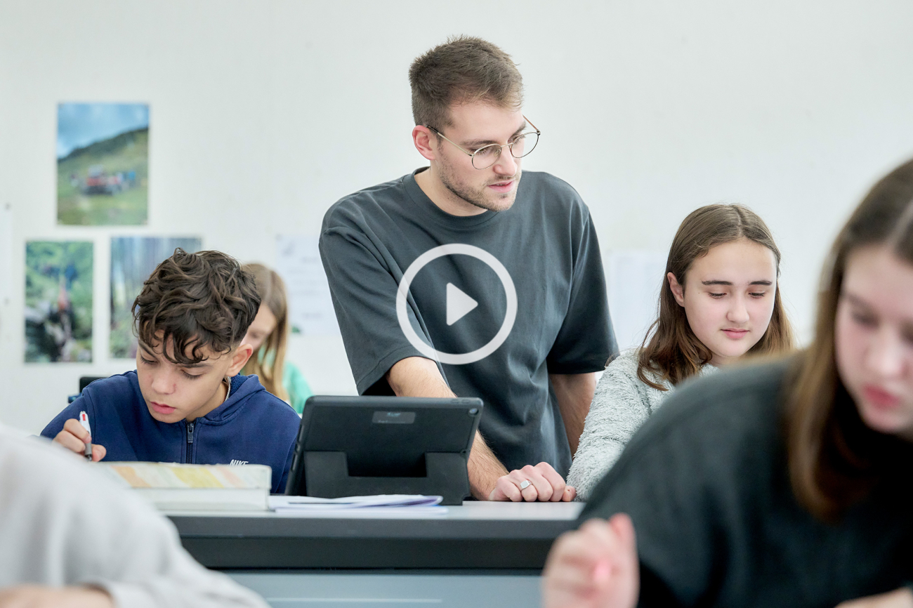 Junger Lehrer erklärt Lernenden etwas im Klassenzimmer