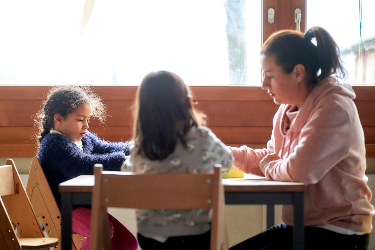 Betreuungsperson mit zwei Kindern am Basteltisch