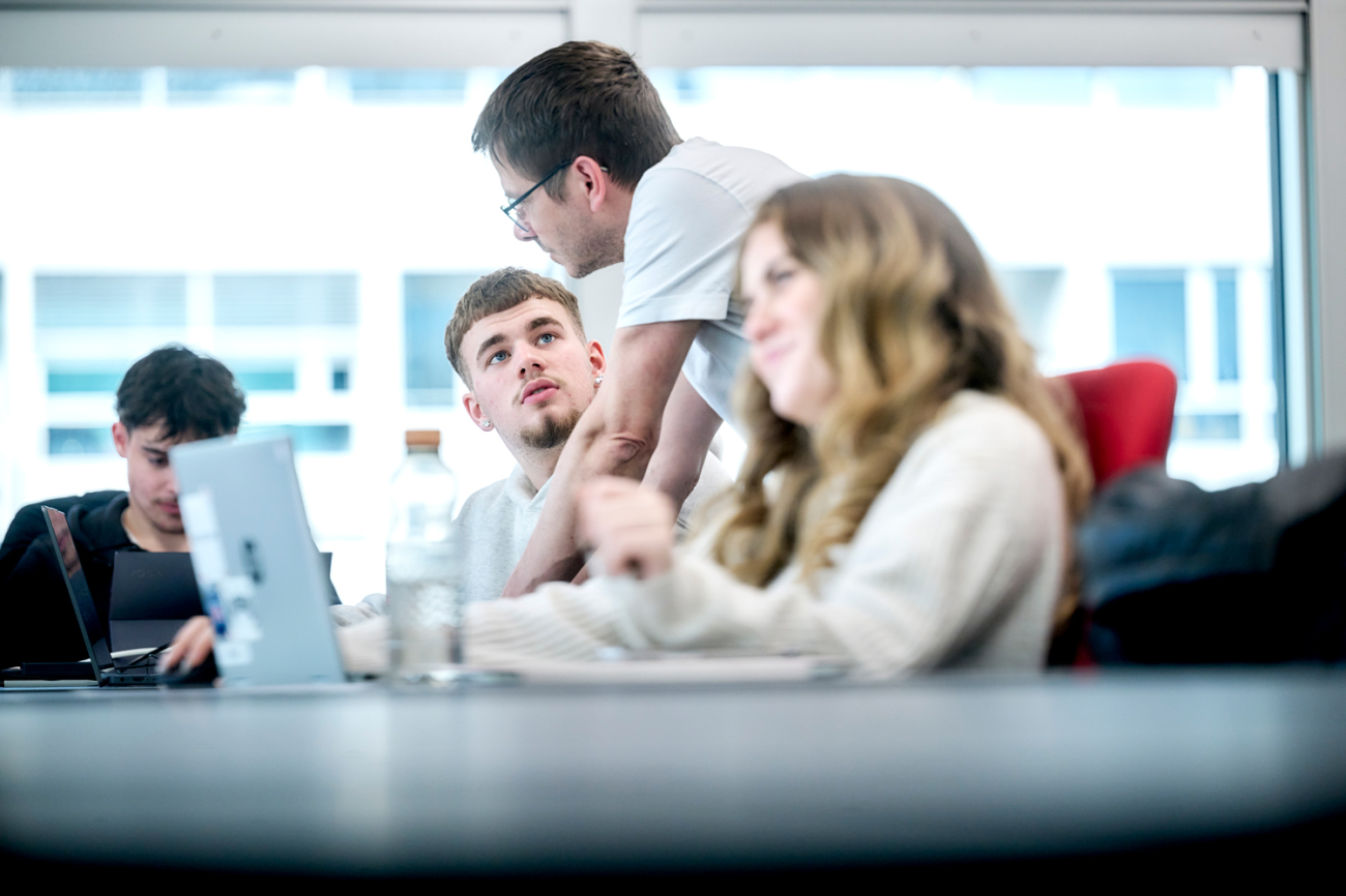 Mann spricht mit Schüler, der hinter Laptop sitzt