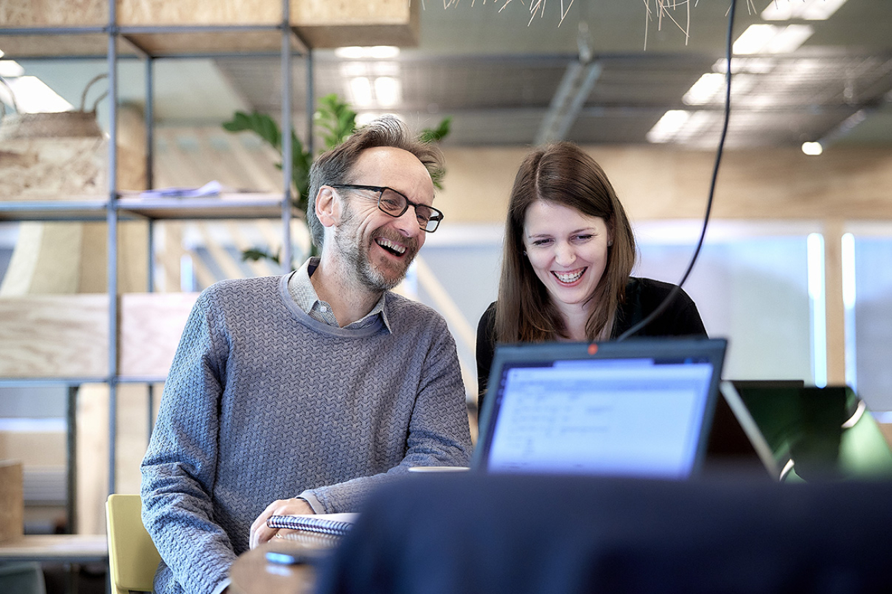 Mann und jüngere Frau sitzen lachend zusammen, ein Laptop ist zu sehen