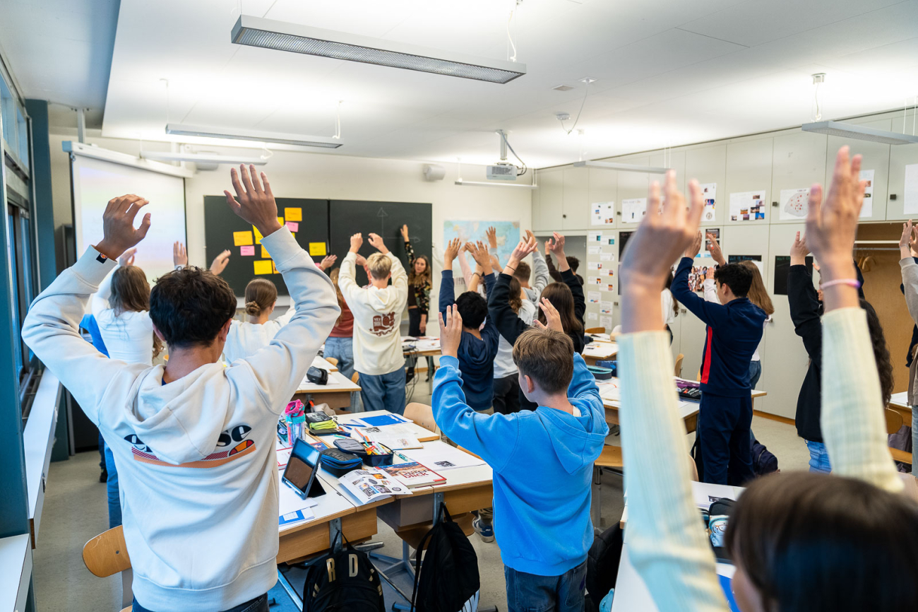 Jugendliche stehen im Klassenzimmer mit erhobenen Händen