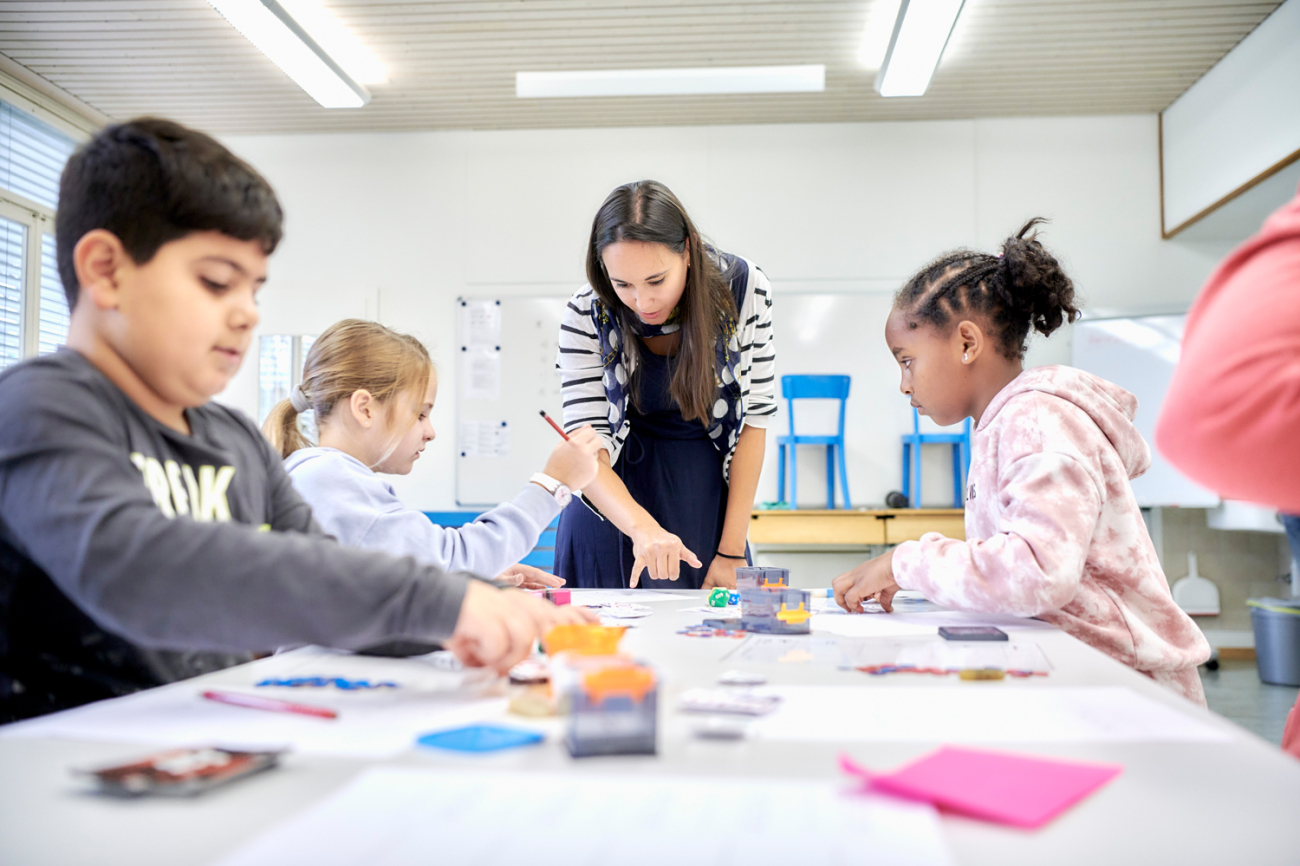 Kinder mit Lehrerin an Gruppenpult