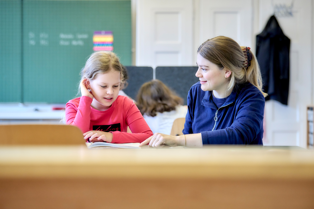 Junge Lehrerin erklärt einem Mädchen etwas am Pult