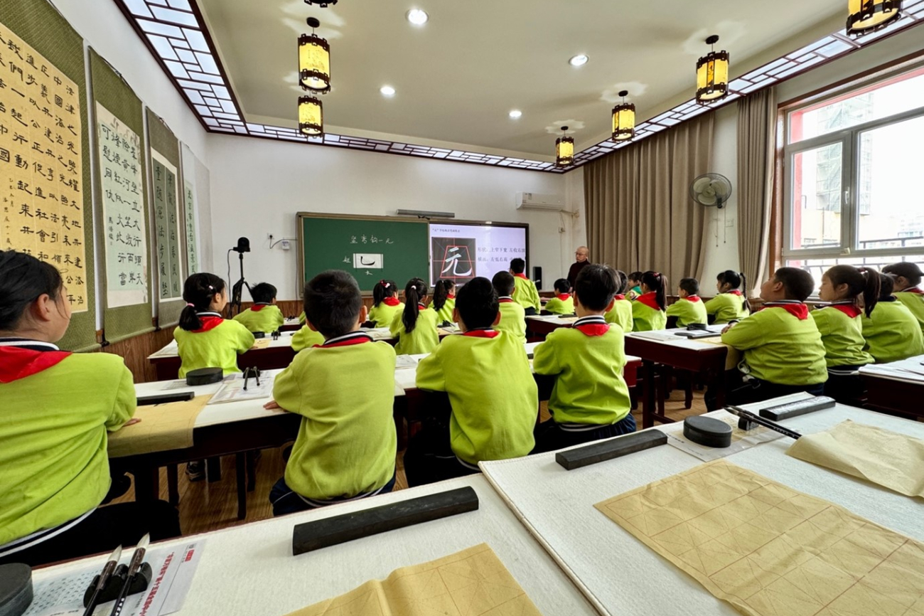 chülerinnen und Schüler in gelben Uniformen von hinten, grosses Klassenzimmer, Tafel vorne.