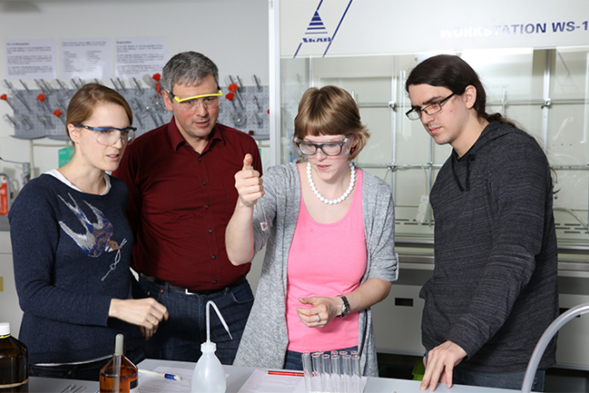Studierende und ein Dozent des Instituts Sekundarstufe II beim Fachdidaktikseminar. Sie befinden sich in einem Labor und tragen Schutzbrillen. Eine Studentin hält eine Pipette in der Hand