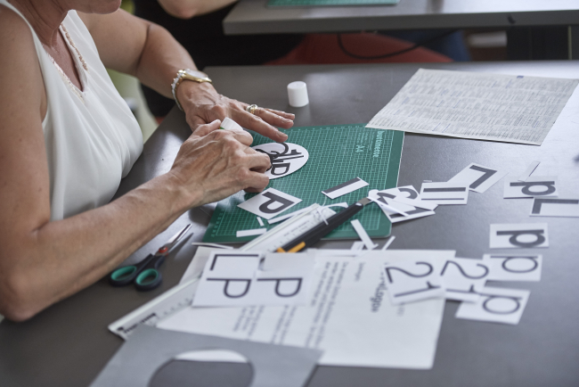 Eine Person, die an einem Pult mit Papier, auf dem Lehrplan 21 steht, bastelt.