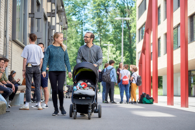 Eine Studentin und ein Student auf dem Hochschul-Real vonRoll. Der Student schiebt einen Kinderwagen.