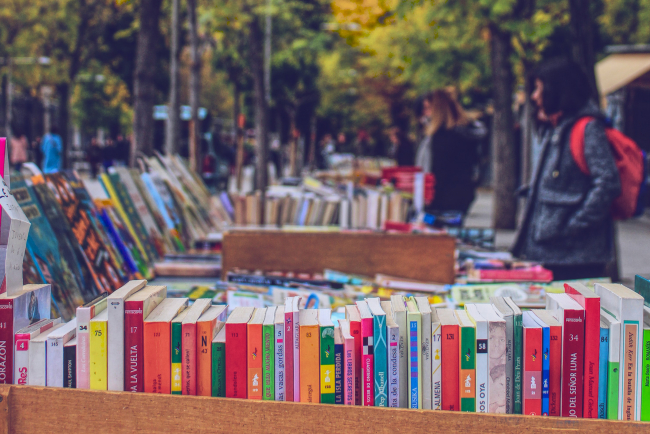 Blick auf einen Büchermarkt mit Bücherkisten im Vordergrund und Besuchenden rechts.