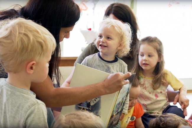 Eine Leiterin erklärt den Vorschulkindern ein Bilderbuch.