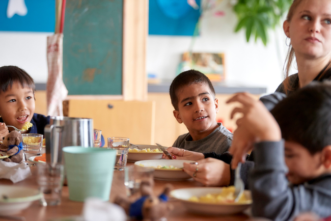 Betreuungsperson in Tagesschule am Mittagstisch mit Kindern