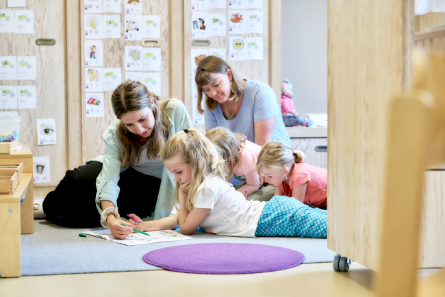 zwei Frauen knien am Boden bei Kindergartenmädchen