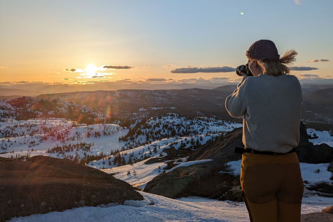 Frau von hinten fotografiert Sonnenuntergang in Schneelandschaft