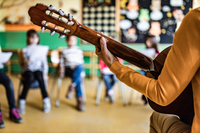 Detailaufnahme einer Hand an der Gitarre, im Hintergrund Schulkinder
