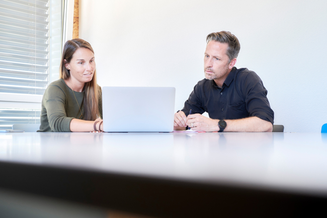 Frau berät Mann an Labtop, sitzend an einem Tisch