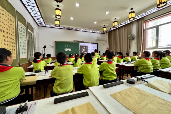 chülerinnen und Schüler in gelben Uniformen von hinten, grosses Klassenzimmer, Tafel vorne.