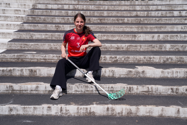 Studentin sitzt auf der Treppe mit einem Unihockey-Schläger.