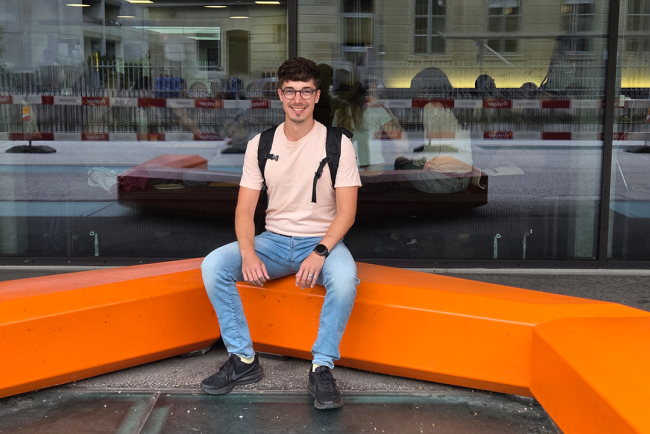 Ein Student sitzt auf einer orangen Bank