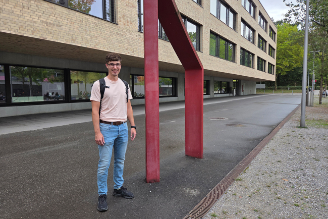 Ein Student steht neben dem Hochschulgebäude.