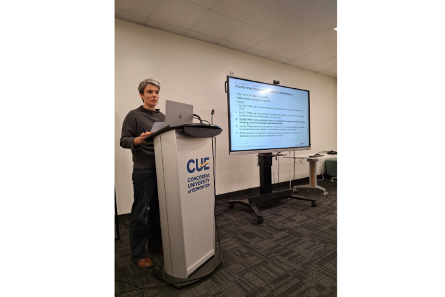 Nina Simonett steht an einem Rednerpult der Concordia University of Edmonton und hält eine Präsentation vor einem grossen Bildschirm.